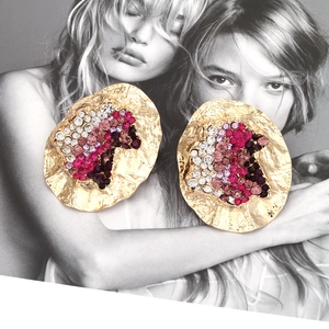 Chunky irregular round gold earrings with colorful rhinestones on a fashion magazine background