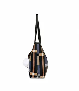 Side view of large plaid tote bag with plush ball charm and colorful ribbon detail
