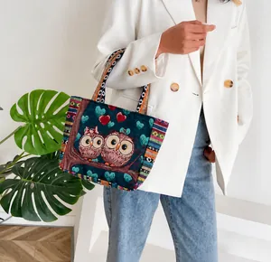 Detailed embroidery of owls on a navy canvas tote bag held by a model in a blazer