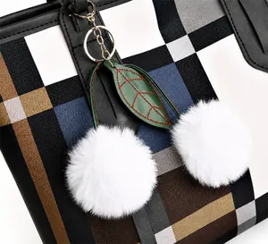 Detail of plaid handbag showing soft white pom-poms and green leaf pendant with gold hardware