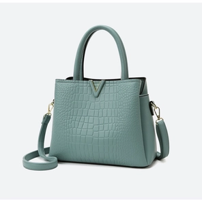 Detail view of crocodile-patterned turquoise handbag with golden V-shaped metal hardware