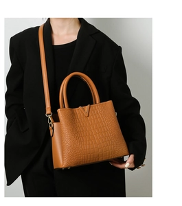 Detail of brown crocodile pattern leather handbag with gold V-shape buckle on model