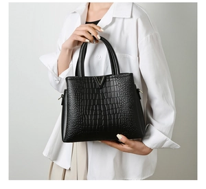 Close-up of black crocodile pattern leather handbag with metallic V-shaped buckle detail