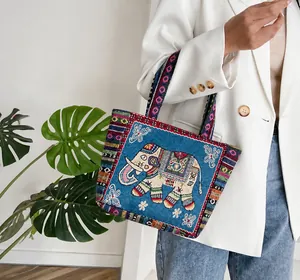Primer plano del bolso étnico azul oscuro con bordado de elefante dorado y asas de tejido trenzado