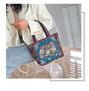 Detailed embroidery of an elephant on a blue canvas tote bag with woven handles