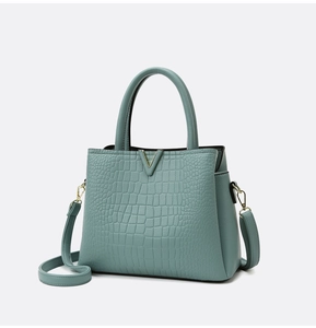 Close-up of mint green crocodile embossed leather handbag with golden V-shaped metal hardware