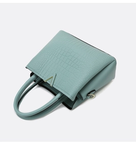 Detail of mint green crocodile embossed leather handbag with golden V-shaped metal hardware
