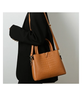 Detail of caramel crocodile embossed texture and V-shaped metal buckle on handbag
