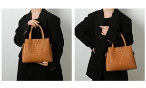 Detail of brown crocodile embossed handbag featuring a stylish gold V-shaped metal logo