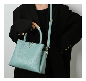 Detail of mint green crocodile embossed tote bag with gold V-hardware on model