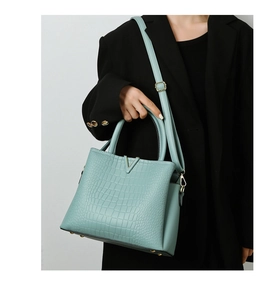 Detail of mint blue crocodile embossed handbag with gold V-decoration and leather texture
