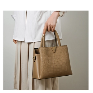 Close-up of khaki crocodile pattern handbag with gold V-hardware held by a model