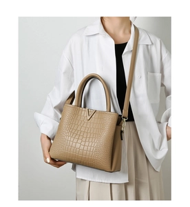Brown crocodile embossed tote bag with V-shaped metal hardware worn by a fashion model
