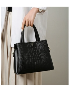 Close-up of black crocodile pattern leather handbag with gold V-shaped metal hardware