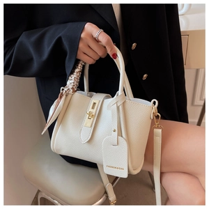 Détail d'un sac en cuir blanc avec boucle dorée, foulard imprimé et étiquette mode