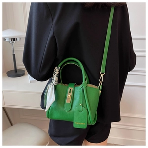 Détail du sac en cuir vert avec une élégante écharpe florale nouée sur la poignée supérieure