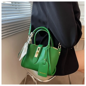 Sac seau en cuir vert avec fermoir doré et foulard porté sur un blazer noir chic