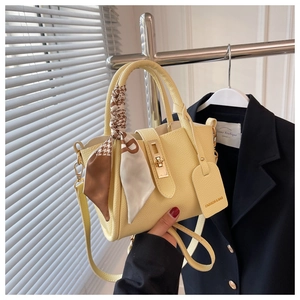 Détail macro du sac en cuir jaune avec fermoir doré et poignée ornée d'un foulard en soie