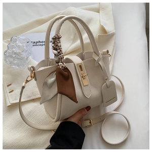 Détail du sac seau crème en cuir grainé avec fermoir doré et foulard en soie sur l'anse