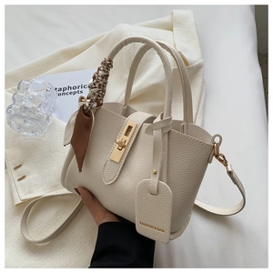 Détail du sac seau blanc cassé avec serrure dorée et foulard décoratif en soie sur la poignée
