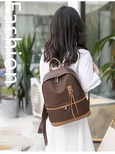 Outdoor back view of a minimalist brown nylon backpack with leather tassels and top handle