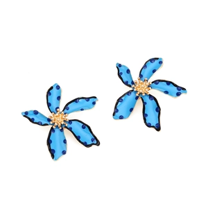 Detail of blue floral earrings with black polka dots and a textured golden flower core