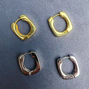 Gros plan de boucles d'oreilles créoles carrées en or et argent sur cuir bleu foncé