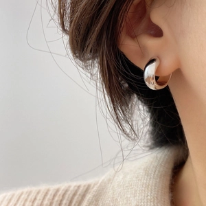 Close-up of minimalist polished silver C-shaped hoop earring on ear for women