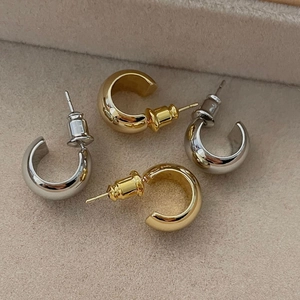 Close-up of gold and silver C-shaped bean earrings on a soft jewelry display tray