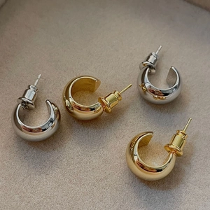 Polished 18K gold and silver C-shaped stud earrings displayed on a beige velvet surface