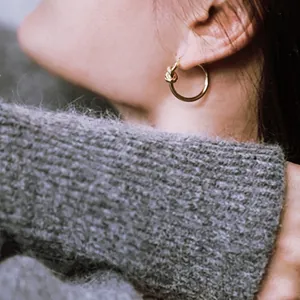 Orecchino a cerchio con nodo dorato minimalista indossato su lobo con maglione elegante