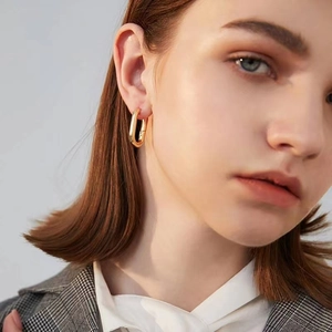 Gros plan d'un modèle portant des boucles d'oreilles créoles carrées en or poli chic