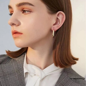 Gros plan de boucles d'oreilles carrées dorées portées par un mannequin en tenue chic