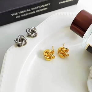 Knotted geometric metal stud earrings in gold and silver finishes, shown on a white ceramic plate