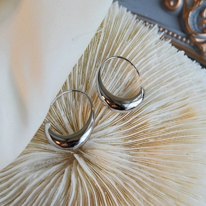Polished silver teardrop hoop earrings on white coral stone background with silk fabric