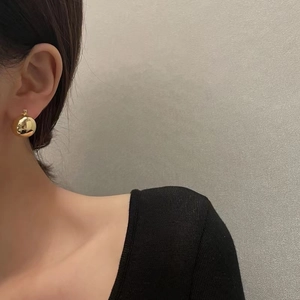 Close-up of elegant 18K gold polished sphere earrings worn by a model in minimalist style