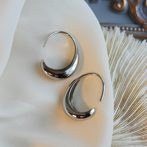 Macro shot of polished silver teardrop earrings resting on white satin fabric