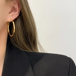 Close-up of a model wearing large golden hollow hoop earrings with a shiny metallic finish