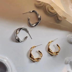 Minimalist twisted C-shaped stud earrings in gold and silver finish with metallic shine