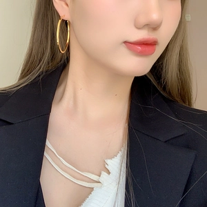 Close-up of model wearing large high-polished gold hoop earrings with a modern sleek finish