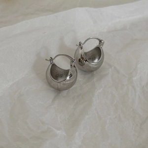 Macro detail of polished silver round ball hoop earrings on white textured paper