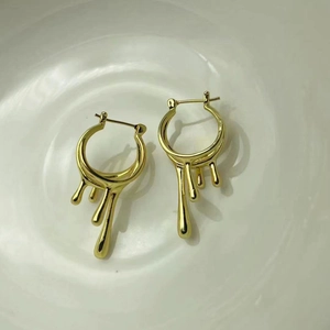 Boucles d'oreilles créoles dorées texture lave irrégulière présentées dans un bol