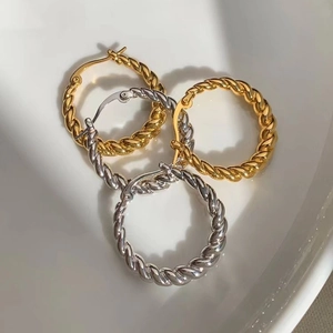 Close-up of gold and silver twisted hoop earrings with 18k plating on a white tray