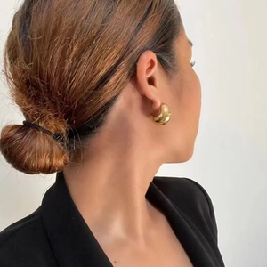 Close-up of a 18K gold-plated chunky C-shaped hoop earring worn on a model's ear