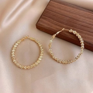 Boucles d'oreilles créoles dorées avec texture métallique sur tissu satiné champagne