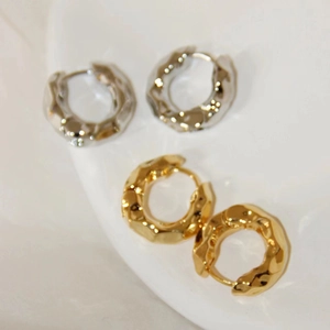 Detailed close-up of gold and silver textured hoop earrings on a white ceramic surface
