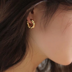 Detailed view of women wearing gold textured hoop earrings with a hammered metal surface