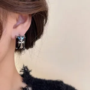 Gothic style black square stud earrings with silver cross detail worn by a model