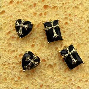 Close-up of gothic gold cross reliefs on black heart and rectangular jewelry charms