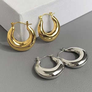 Gros plan de boucles d'oreilles créoles épaisses en U en fini métallique or et argent